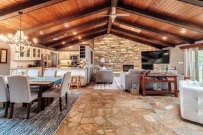 Step inside this stunning open-concept retreat featuring tall wood-beamed ceilings, rustic stone flooring, and a spacious layout that seamlessly connects the kitchen, dining, and living areas—perfect for gathering, relaxing, and making memories.