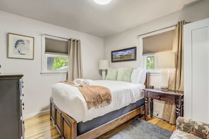 Primary bedroom with a plush bed, soft lighting, and dual windows that bring in fresh air and gentle morning sun.