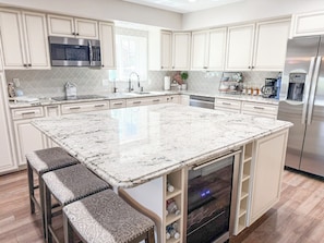 Cook with ease in a fully stocked kitchen featuring a large island, stainless appliances, wine fridge, and seating for casual breakfasts or evening snacks.
