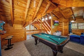 An evening spent in your cabin's fantastic game room, where laughter and friendly rivalry fill the air around the pool table. With its welcoming wood-paneled walls and a dedicated entertainment setup, this is the ultimate spot to unwind and connect with yo