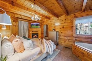 Unwind in this charming log cabin bedroom, featuring a cozy fireplace, a mounted TV, and a comfortable bed, all set against a backdrop of beautiful wooden walls and ceilings. Enjoy peaceful moments and scenic views from your window, ensuring a restful retr