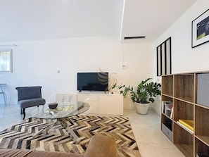 Avec un design moderne, ce salon invite à la détente. Profitez de soirées cinéma confortables grâce au téléviseur, et laissez-vous séduire par l'élégance de la table en verre et du tapis géométrique.