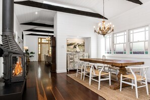 Spacious dining area featuring a rustic timber table, statement chandelier, and cosy fireplace—perfect for family meals or relaxed entertaining in style.