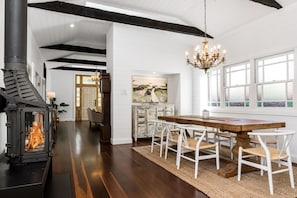Spacious dining area featuring a rustic timber table, statement chandelier, and cosy fireplace—perfect for family meals or relaxed entertaining in style.