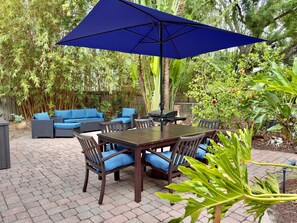 Lush greenery lines the patio, including banana leaves, hibiscus plants, bamboo, and palms, giving the entire space a secluded, garden-like feel.