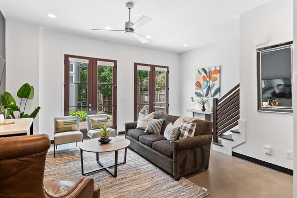 Huge windows and plenty of comfortable seating in the living room with a Smart TV, ceiling fan, and French doors leading out to the community patio & picnic area. The couch doubles as a comfortable Queen pull-out bed.