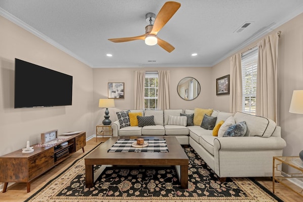 Cozy living room with plush sofa, smart TV, fan & board games for fun.