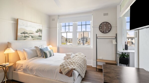A bright and inviting bedroom featuring a comfortable bed with crisp white linens, a plush throw blanket, and decorative pillows. 