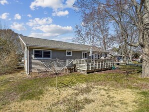 This side view illustrates the spacious outdoor deck, ideal for entertaining, alongside a spacious yard adorned with trees, highlighting the property’s spaciousness and privacy.