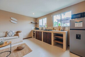 Open kitchen with natural wood cabinetry, full-size fridge, and all the essentials for convenient home cooking.

