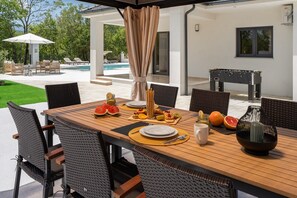 Ein überdachter Außen-Essbereich mit einem großen Tisch und einem Holzkohlegrill für Mahlzeiten im Freien.
