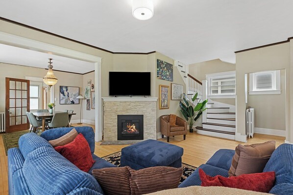 This beautifully designed living room features a plush sectional sofa, a modern electric fireplace, and a large smart TV, creating a warm and inviting atmosphere for families and groups.