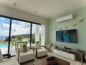 The living room at SeaDream Villa is equipped with a large smart TV, perfect for enjoying your favorite shows or movies in a spacious, comfortable setting with ocean views, making it an ideal spot for relaxation and entertainment.