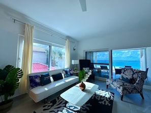 The living room is highlighted by large picture windows that frame stunning views of the ocean, filling the space with natural light and offering a seamless connection to the breathtaking surroundings.