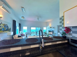 The kitchen is equipped with a sleek bar seating area, offering a casual spot to enjoy meals, drinks, or conversation while taking in the open-concept layout and ocean views.