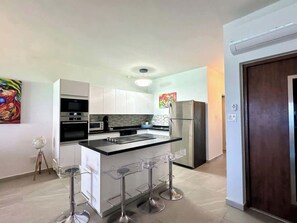 The apartment boasts a modern kitchen equipped with sleek appliances, a spacious island, and four chairs—perfect for casual dining or sharing conversations while cooking.