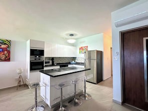 The apartment boasts a modern kitchen equipped with sleek appliances, a spacious island, and four chairs—perfect for casual dining or sharing conversations while cooking.