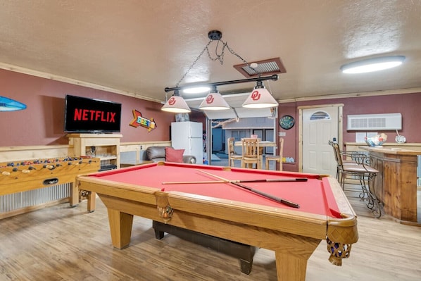 Garage game room with pool table, foosball, cornhole, and bar area