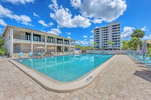 The community pool surrounded by chaise lounges and umbrella tables. The community center and the unit building.