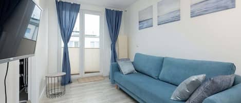 A bright living room featuring a blue corner sofa, modern decor, and large windows dressed with blue curtains.