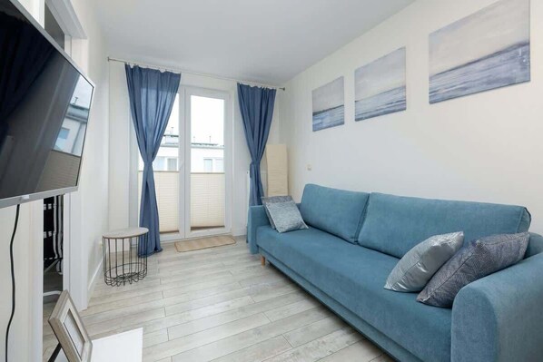 A bright living room featuring a blue corner sofa, modern decor, and large windows dressed with blue curtains.