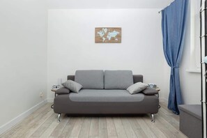 A cozy bedroom with a gray sofa bed, blue curtains, and a minimalist wall painting.