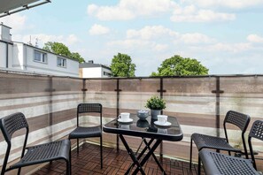 A private outdoor terrace featuring a square table and black chairs, surrounded by a wooden privacy fence and greenery.