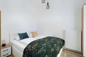A bright bedroom featuring a double bed with green floral bedding and minimalist decor.