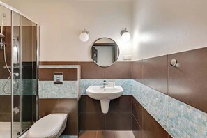A pristine bathroom featuring a walk-in glass shower and dark-toned tiles. A white vanity with a circular mirror completes the polished look.