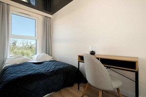 A neatly made bedroom with a soft beige wall, large window, and comfortable double bed.