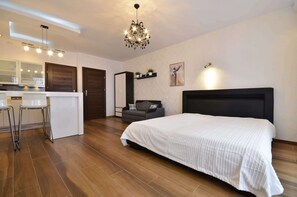 Another perspective of the bedroom area with a double comfortable bed connected to the kitchenette. A sofa is visible against the wall.