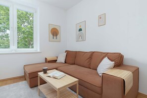 A simple living room setting with a coffee table, brown sofa, and white walls with soft decor.

