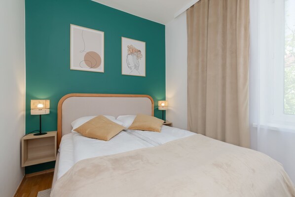 A cozy bedroom featuring a double bed with neutral bedding, green accent wall, and framed minimalist art above the headboard.