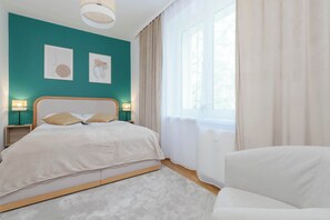 A bright bedroom with a teal accent wall, beige curtains, and a modern white bed with warm lighting from both sides.