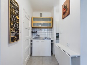 A compact kitchen with white cabinets, wooden countertops, and modern appliances. It is a simple and functional cooking space with a small piece of artwork on the wall.