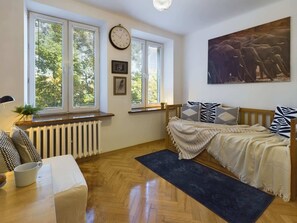 Another view of the same bedroom, showing the bed and a sitting area by the windows. The room is filled with natural light, and a small radiator is visible under the windows.