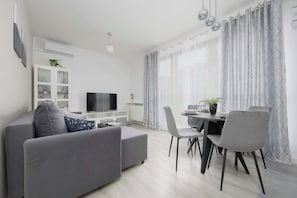 A corner of the living room showing a TV mounted on the wall above a white console. The seating area looks comfortable and inviting.