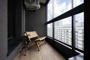 The balcony is equipped with a wooden chair and table, creating a place to relax. The entire area is sheltered by a functional glass enclosure, which protects it from adverse weather conditions.