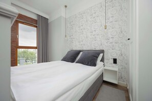 A serene bedroom featuring a gray and white color palette, decorative wallpaper, and a bedside lamp on a floating shelf.