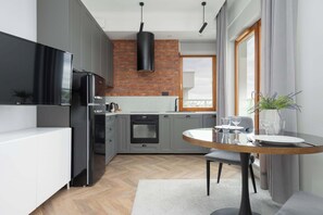 A functional kitchen with white upper cabinets, black lower ones, a brick wall, and wood flooring.