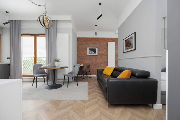 A stylish living area with a dark sofa, yellow cushions, a dining table, and brick accent walls giving it a modern, industrial feel.