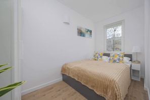 A second bedroom with a comfortable double bed, modern artwork, and beige curtains.