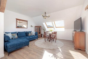A different angle of the living room, showing a large wooden dining table, comfortable seating, and decorative lighting.