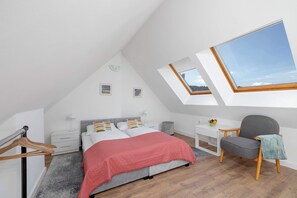The first bedroom features a double bed with pink bedding, wooden furniture, and a skylight window allowing natural light to brighten the space.