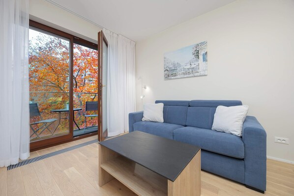 Bright and comfortable living room with blue double sofa bed, coffee table, television, and dining table with chairs.