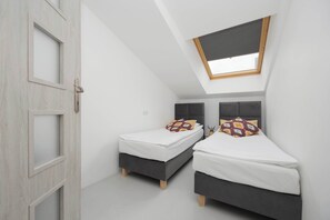 A cozy attic bedroom with two single beds under a slanted ceiling and a skylight window.