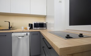 A compact kitchen space with white cabinets, wooden countertops, and modern appliances.