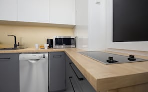 A compact kitchen space with white cabinets, wooden countertops, and modern appliances.