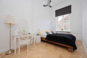 Bedroom with a double bed with linens and a dark bedspread. The room also has a dressing table with a mirror and a chair.