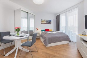 A cozy living area with a grey double bed, a dining table, and floor-to-ceiling windows.